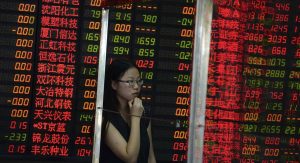 A Chinese woman stands behind a glass panel near stock prices displayed on a board at a brokerage house in Shanghai, China, Monday July 6, 2015. Shares in big Chinese state companies rose Monday following weekend promises of government action to halt a slide in stock prices but many others sank as jittery small investors looked for ways to cut their losses. (Chinatopix Via AP) CHINA OUT